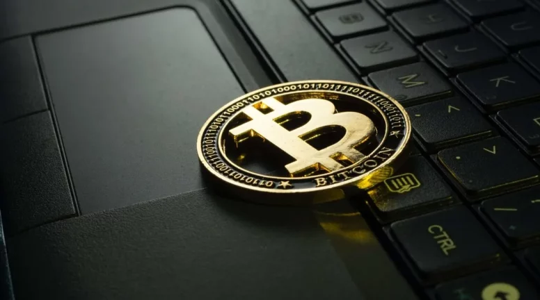 A physical Bitcoin sitting on a laptop.