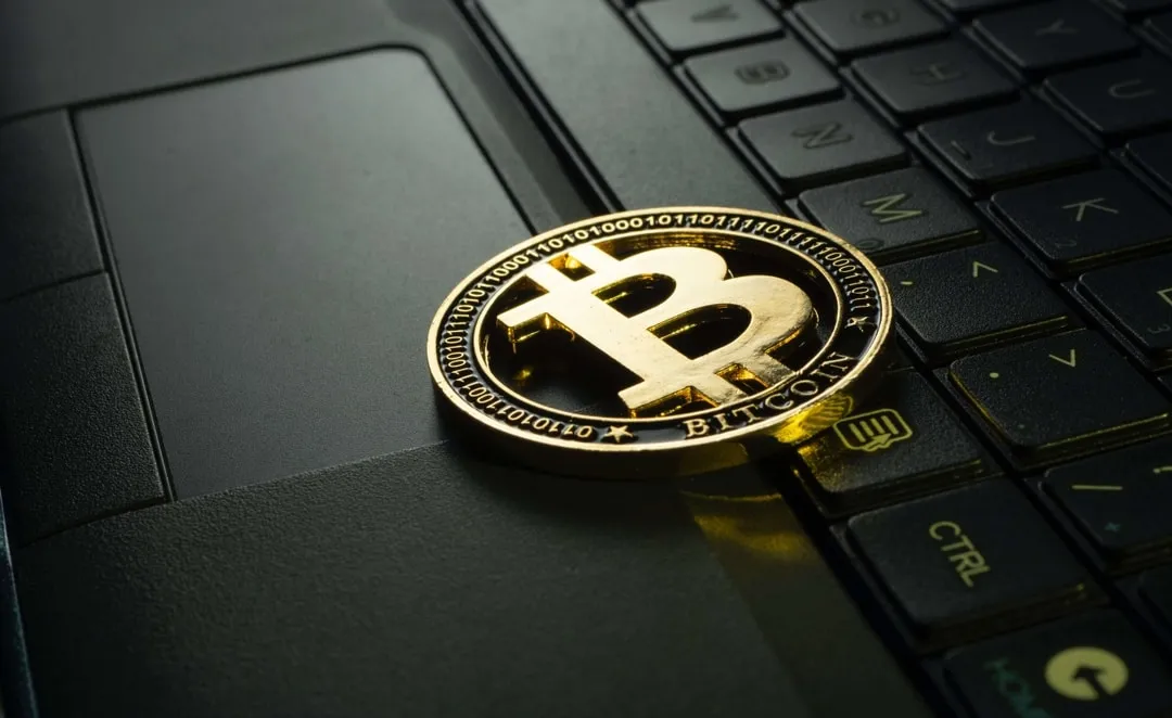 A physical Bitcoin sitting on a laptop.